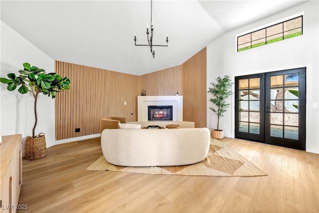 living area with wood finished floors, a lit fireplace, high vaulted ceiling, a chandelier, and wooden walls