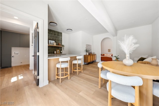 dining space featuring light wood finished floors, arched walkways, baseboards, and beam ceiling
