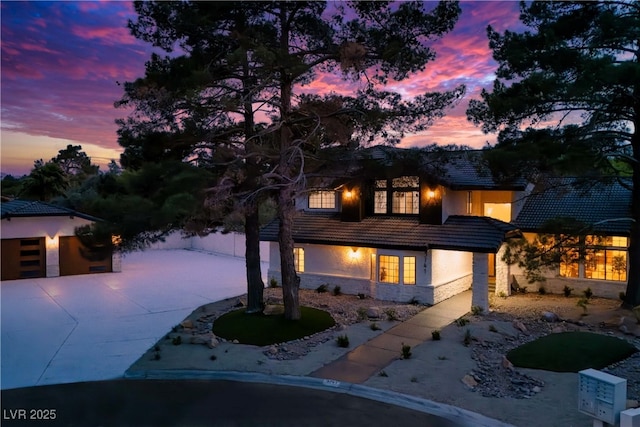 view of front facade featuring stucco siding, a tiled roof, concrete driveway, and stone siding