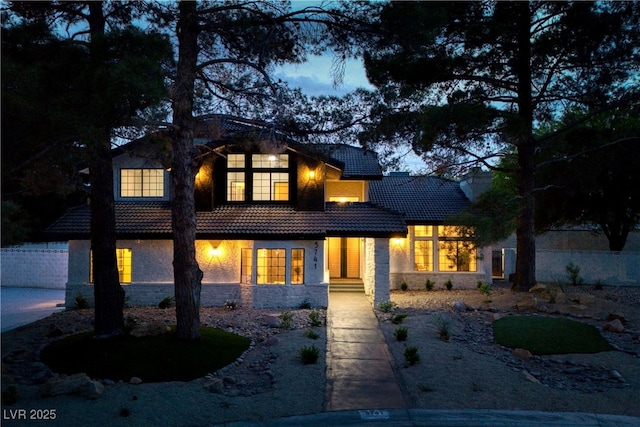 rear view of property with a tiled roof, stone siding, stucco siding, and fence