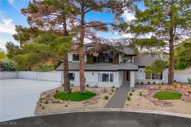 view of front of house featuring stone siding, stucco siding, fence, and a tile roof