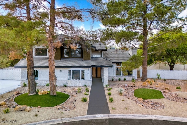 view of front of house featuring a tile roof, fence, stone siding, and stucco siding