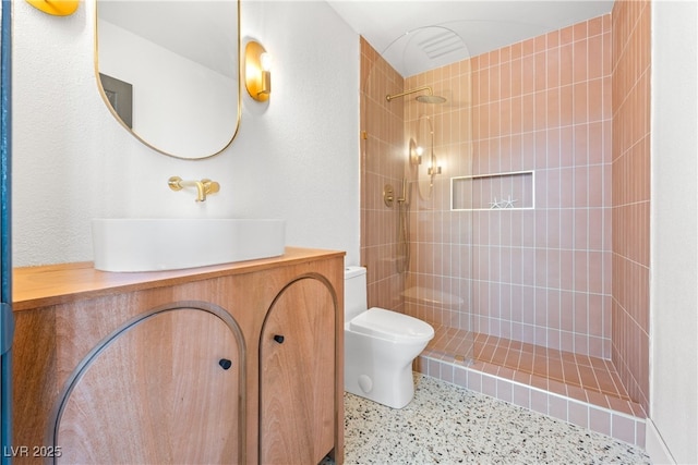 full bathroom with toilet, tiled shower, vanity, and speckle patterned floor