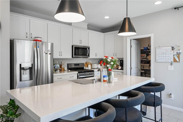 kitchen with appliances with stainless steel finishes, light countertops, a kitchen bar, baseboards, and white cabinets