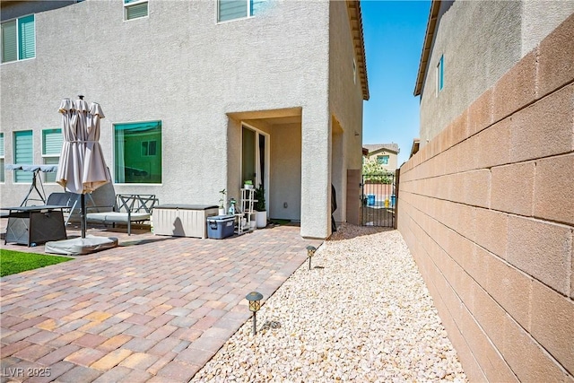 rear view of house with stucco siding, a patio, a gate, and fence