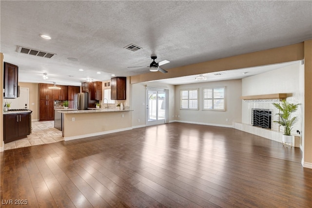 6117 Foxcroft Ave, Las Vegas, NV 89108 - unfurnished living room with a ceiling fan, light wood-style flooring, a textured ceiling, a tile fireplace, and baseboards