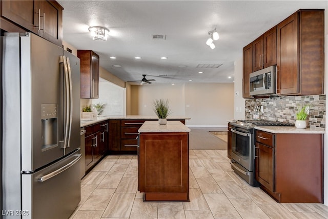 6117 Foxcroft Ave, Las Vegas, NV 89108 - kitchen with appliances with stainless steel finishes, a ceiling fan, backsplash, a peninsula, and a kitchen island