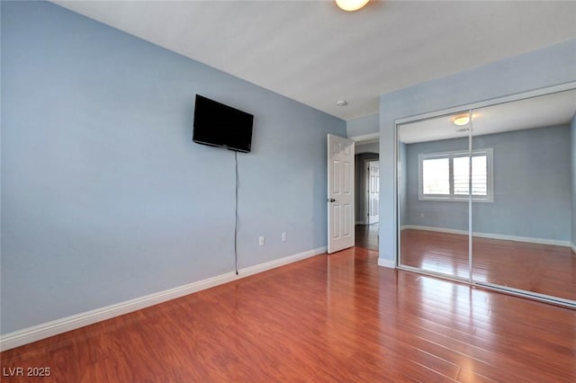 unfurnished bedroom featuring wood finished floors, baseboards, and a closet