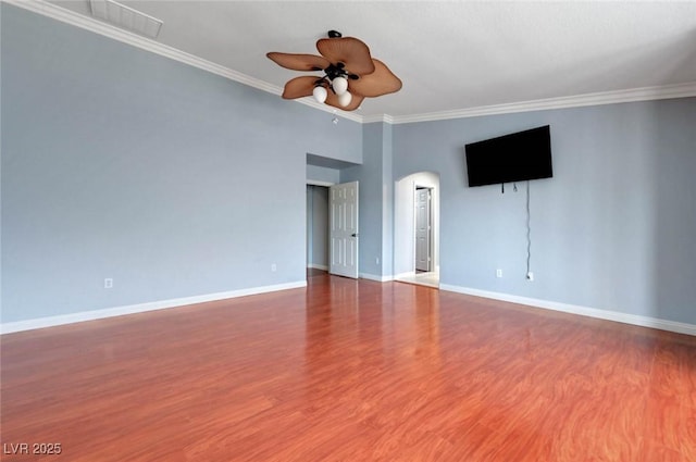 empty room featuring a ceiling fan, baseboards, wood finished floors, crown molding, and arched walkways
