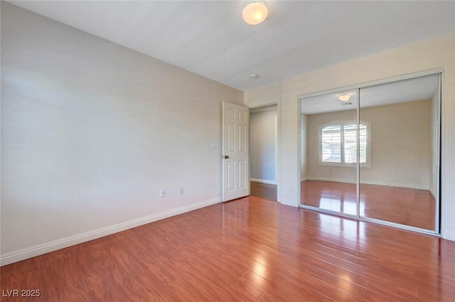 unfurnished bedroom with baseboards, wood finished floors, and a closet