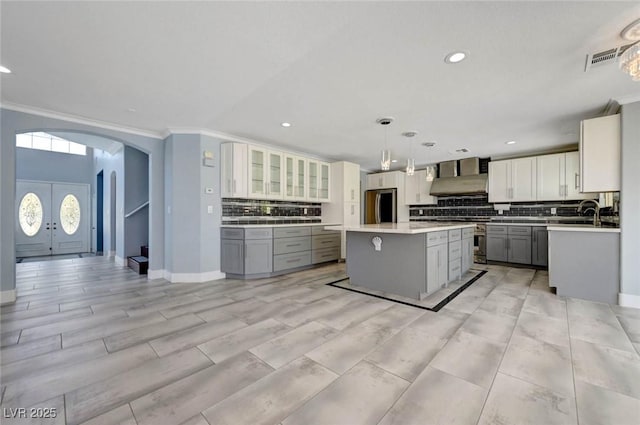 kitchen featuring appliances with stainless steel finishes, arched walkways, a kitchen island, crown molding, and tasteful backsplash