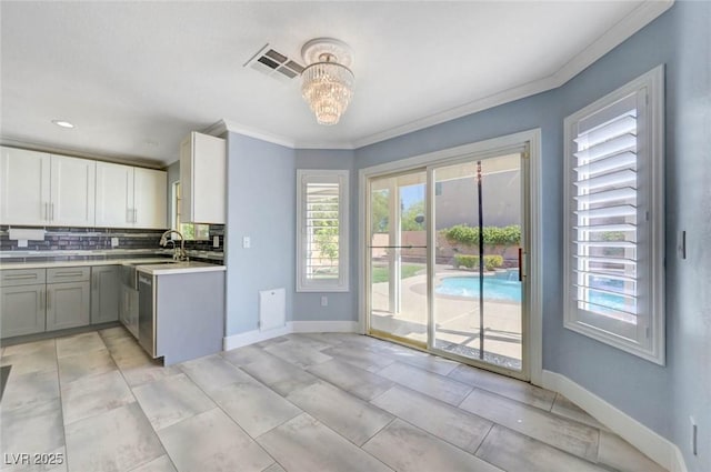 kitchen featuring baseboards, decorative backsplash, ornamental molding, a chandelier, and light countertops