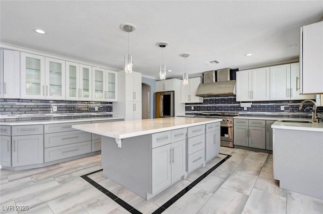 kitchen featuring stainless steel appliances, wall chimney exhaust hood, a sink, arched walkways, and gray cabinets