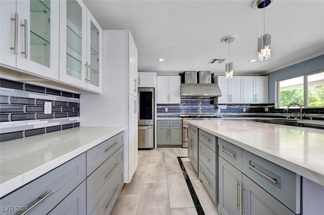 kitchen featuring gray cabinets, wall chimney range hood, backsplash, stainless steel appliances, and hanging light fixtures