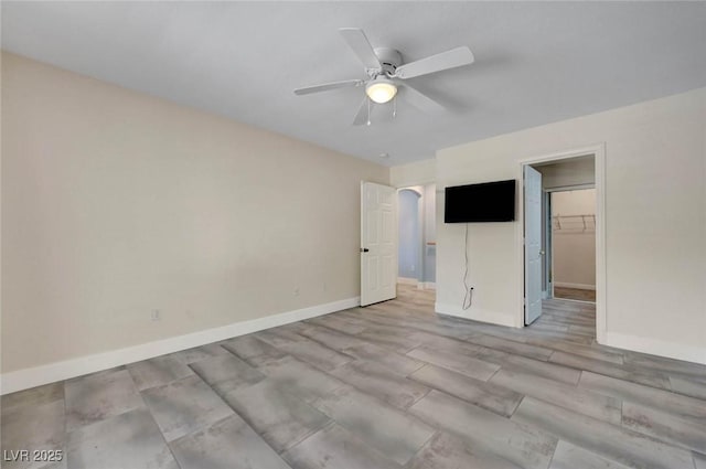 unfurnished bedroom with a walk in closet, baseboards, a ceiling fan, and a closet