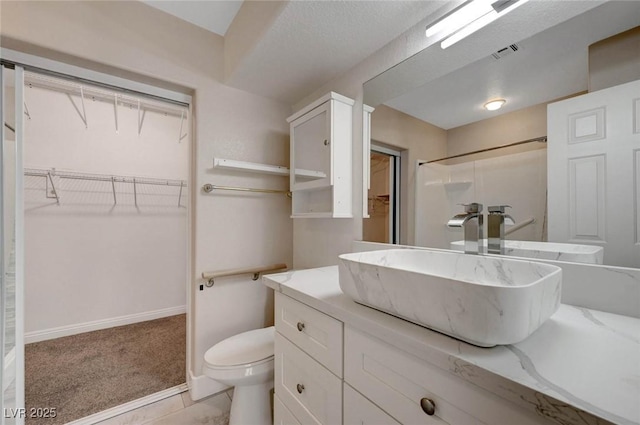 full bath featuring vanity, toilet, a walk in closet, baseboards, and a shower