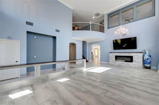 unfurnished living room featuring arched walkways, a towering ceiling, baseboards, a chandelier, and a glass covered fireplace
