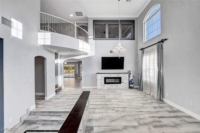281 Powerbilt Ave, Las Vegas, NV 89148 - unfurnished living room featuring crown molding, a towering ceiling, arched walkways, a chandelier, and baseboards