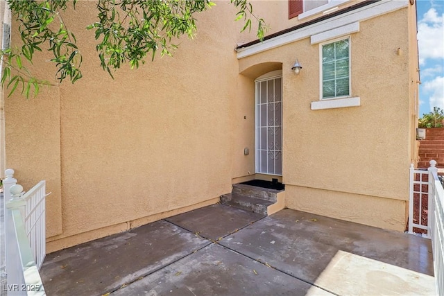 entrance to property featuring a patio area, stucco siding, and fence