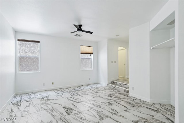 unfurnished room with marble finish floors, arched walkways, ceiling fan, and baseboards