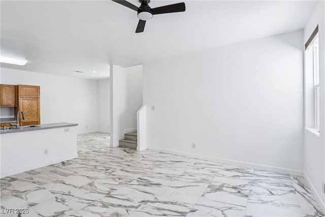 unfurnished living room with a sink, a ceiling fan, light marble finish floors, baseboards, and stairway