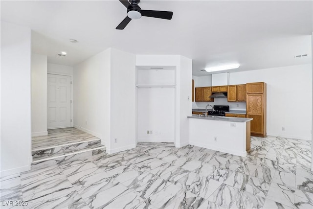 kitchen featuring brown cabinets, ceiling fan, under cabinet range hood, black range with gas stovetop, and a peninsula