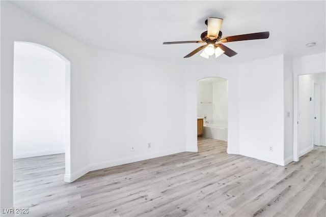 unfurnished room with arched walkways, light wood finished floors, ceiling fan, and baseboards