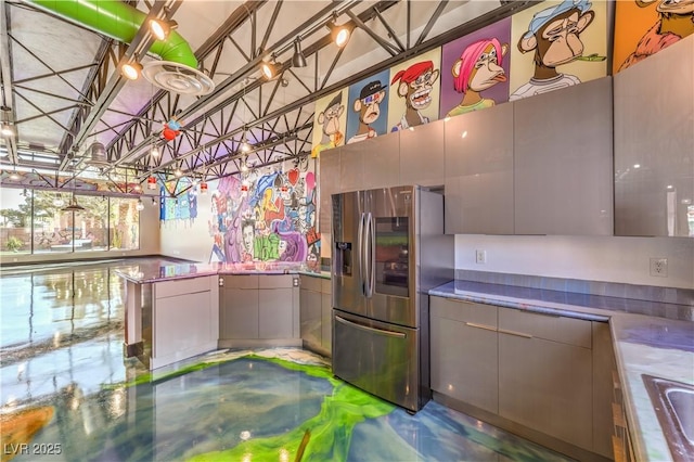 kitchen featuring stainless steel refrigerator with ice dispenser, gray cabinets, concrete flooring, and a sink