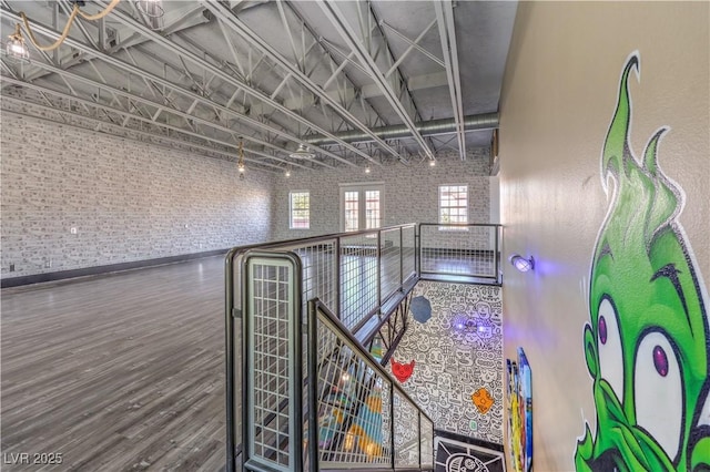 corridor with wood finished floors, baseboards, brick wall, and an upstairs landing