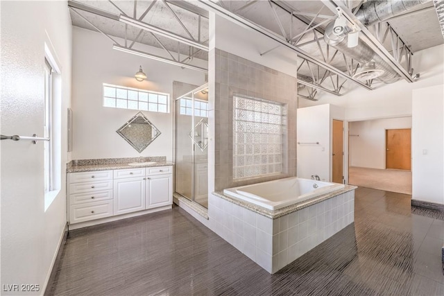 bathroom with a stall shower, vanity, a bath, and baseboards