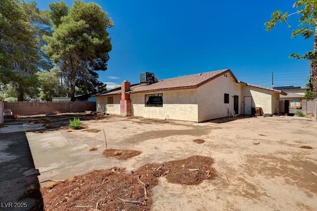 rear view of house with fence, stucco siding, a tiled roof, central AC unit, and a chimney