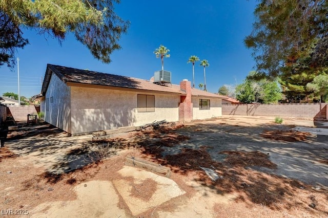 back of property featuring fence, stucco siding, central AC unit, and a chimney