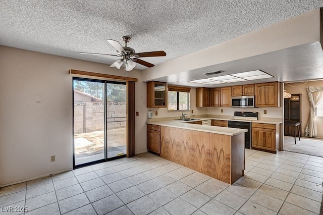 kitchen featuring range with electric stovetop, stainless steel microwave, a peninsula, light countertops, and a textured ceiling