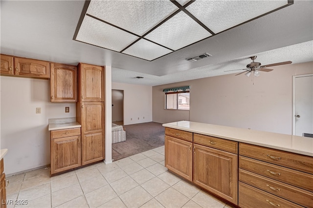 kitchen with light countertops, a ceiling fan, brown cabinets, and light colored carpet