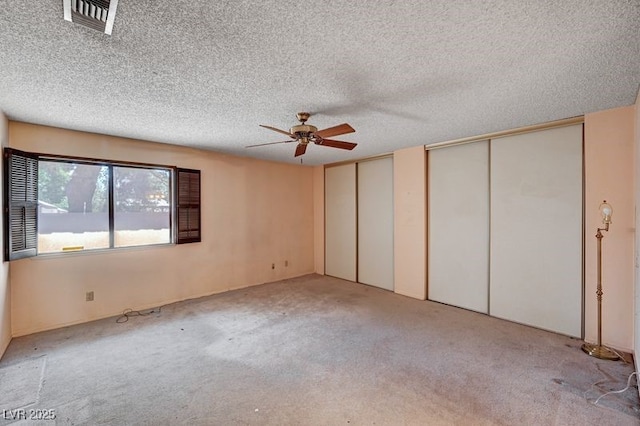 unfurnished bedroom with two closets, carpet flooring, a textured ceiling, and ceiling fan