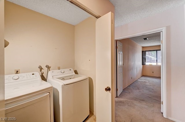 clothes washing area featuring a textured ceiling, washer and clothes dryer, and light colored carpet