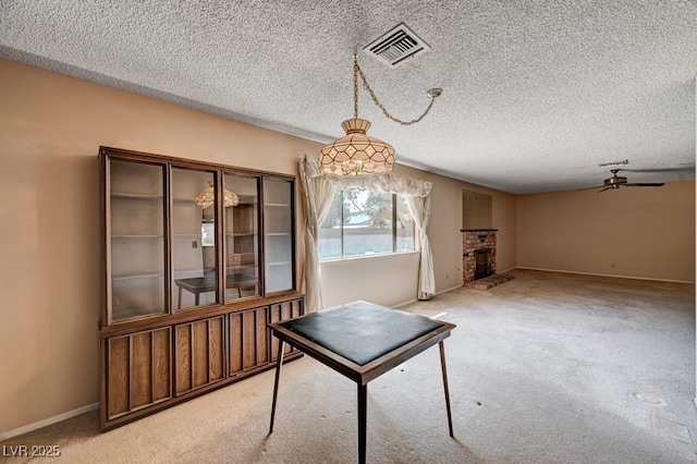 unfurnished dining area featuring carpet, a ceiling fan, baseboards, a textured ceiling, and a brick fireplace