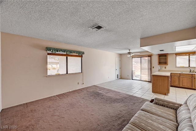living area with ceiling fan, light tile patterned floors, a textured ceiling, baseboards, and light colored carpet