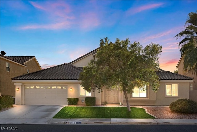 view of front of home featuring a tiled roof, an attached garage, concrete driveway, stucco siding, and a front yard