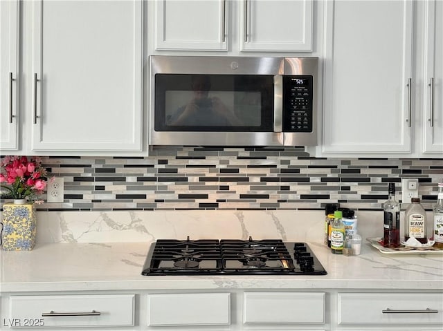 5422 Nestled Moon Ct, Las Vegas, NV 89131 - kitchen featuring stainless steel microwave, white cabinets, black gas stovetop, tasteful backsplash, and light stone countertops