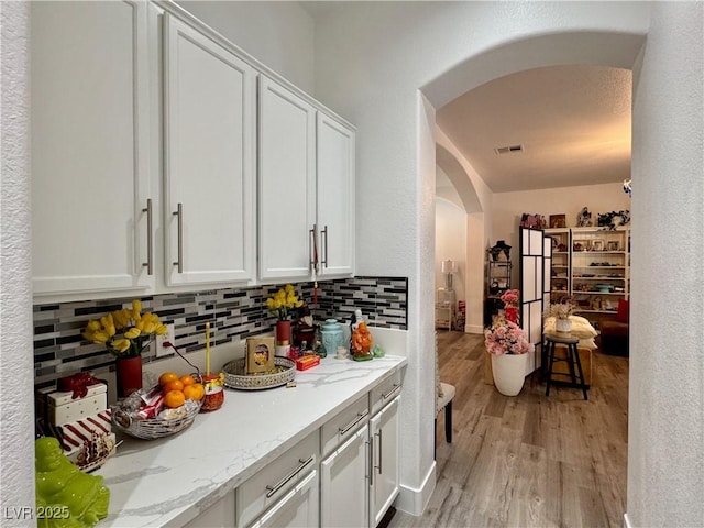 5422 Nestled Moon Ct, Las Vegas, NV 89131 - kitchen featuring arched walkways, tasteful backsplash, light wood-type flooring, white cabinets, and light stone countertops
