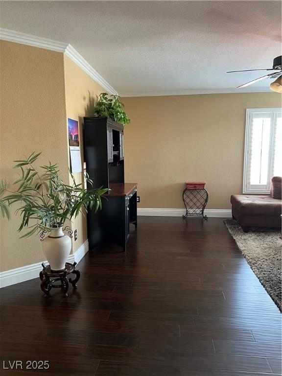 living area featuring crown molding, a ceiling fan, dark wood finished floors, baseboards, and a textured ceiling