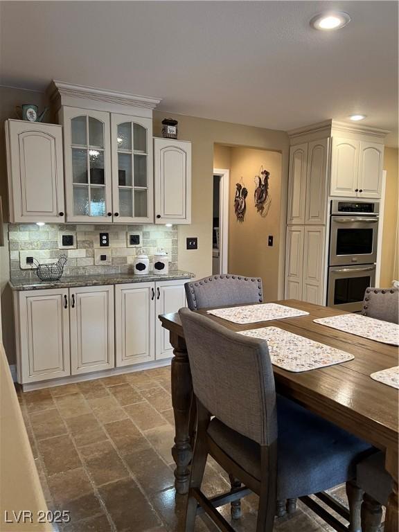 kitchen with double oven, glass insert cabinets, backsplash, stone finish flooring, and recessed lighting