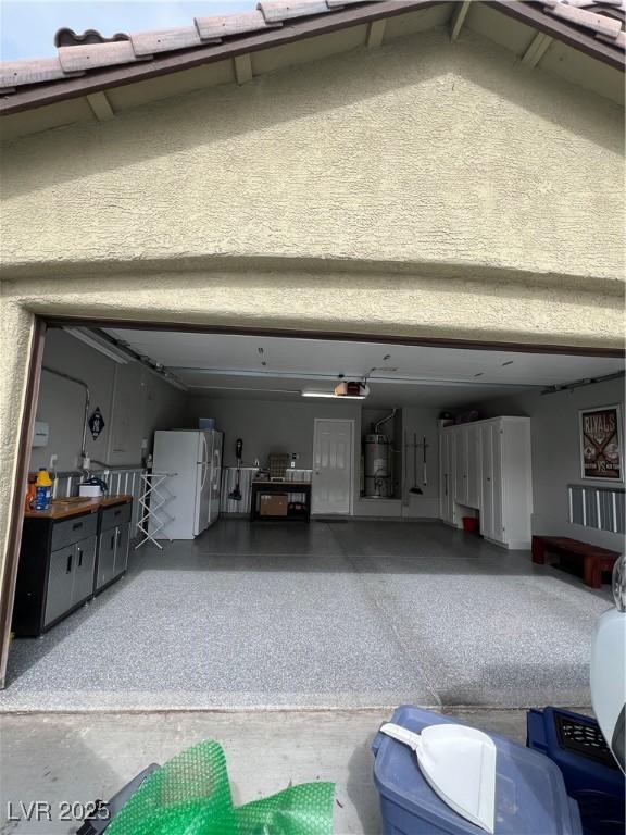 garage featuring freestanding refrigerator, a garage door opener, and strapped water heater