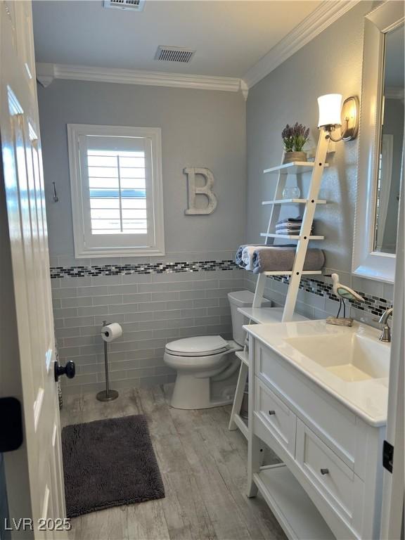 bathroom featuring toilet, ornamental molding, wood finished floors, vanity, and tile walls