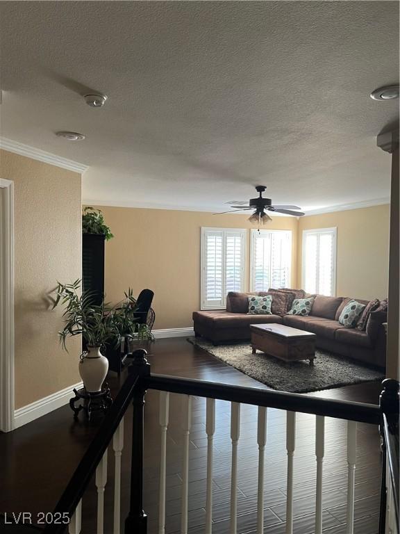 living room featuring baseboards, healthy amount of natural light, crown molding, a textured ceiling, and ceiling fan