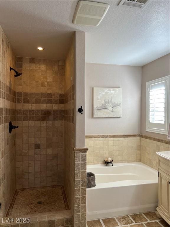 bathroom with a tile shower, a bath, vanity, tile walls, and a textured ceiling