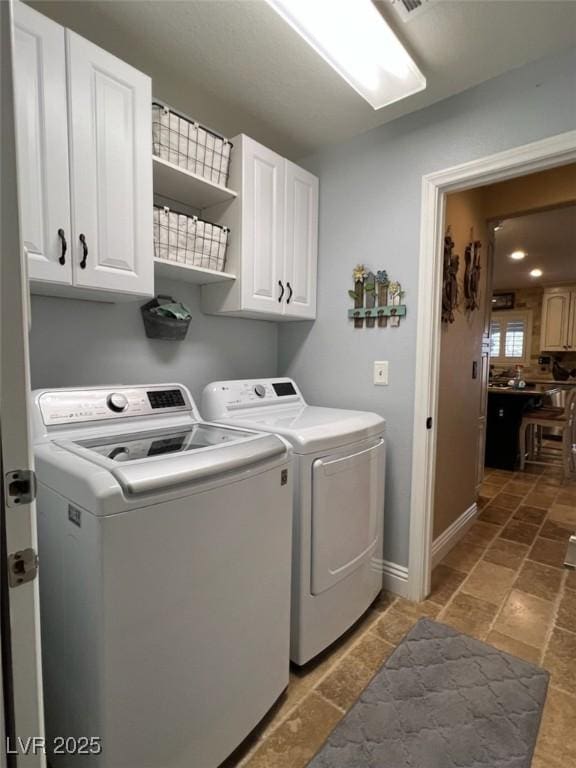 laundry room featuring washer and clothes dryer, cabinet space, baseboards, and stone tile flooring