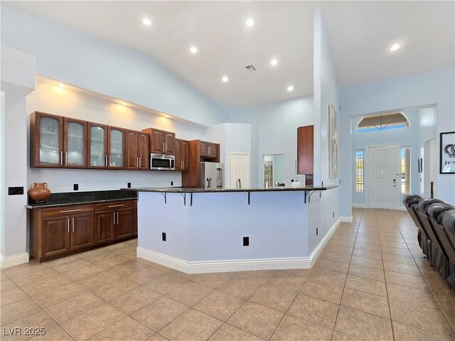 3780 Shawnee Ave, Pahrump, NV 89048 - kitchen featuring appliances with stainless steel finishes, a kitchen breakfast bar, light tile patterned floors, glass insert cabinets, and high vaulted ceiling