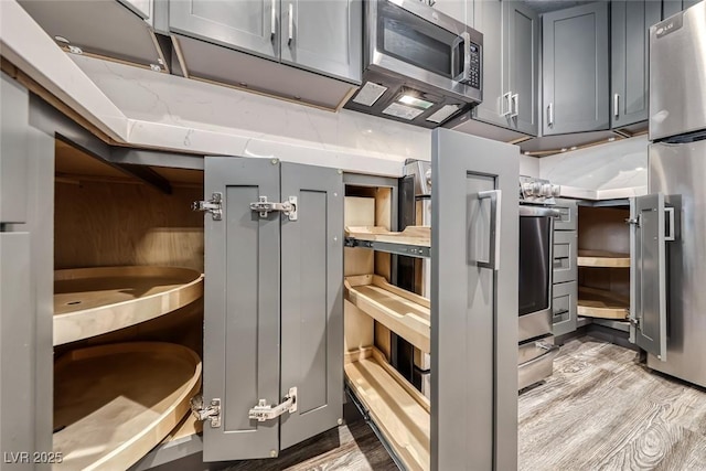 kitchen view of light wood-type flooring, gray cabinets, appliances with stainless steel finishes, and light stone countertops